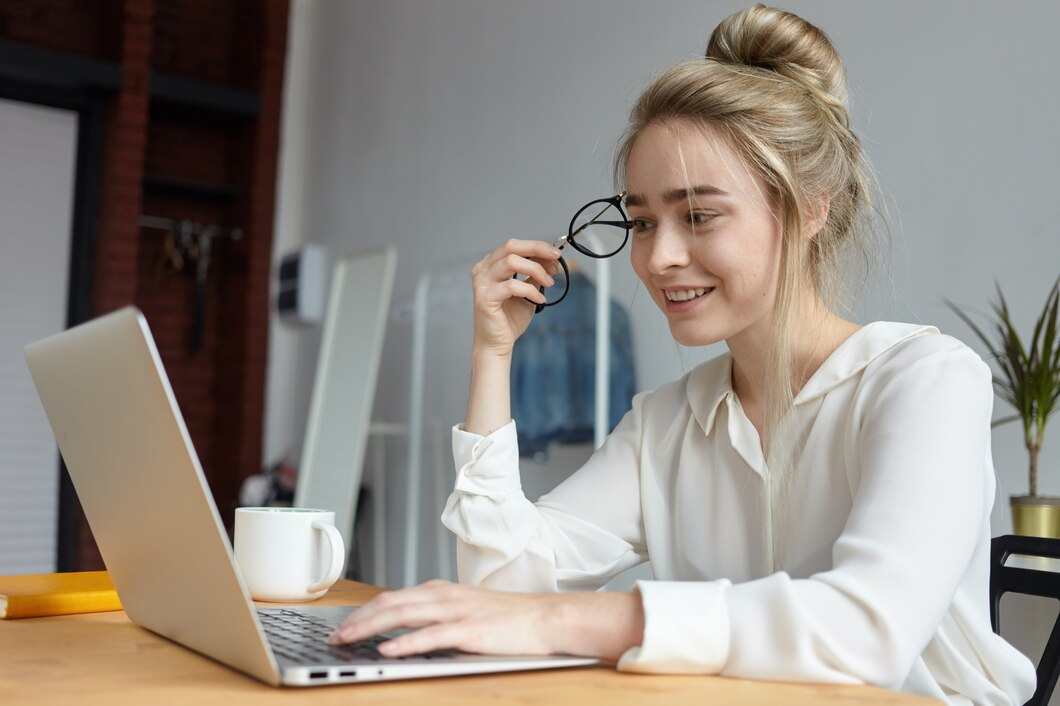modern-technology-gadgets-job-communication-concept-happy-charming-young-woman-with-hair-bun-holding-round-eyeglasses-keyboarding-laptop-pc-browsing-internet-chatting-online_343059-3055